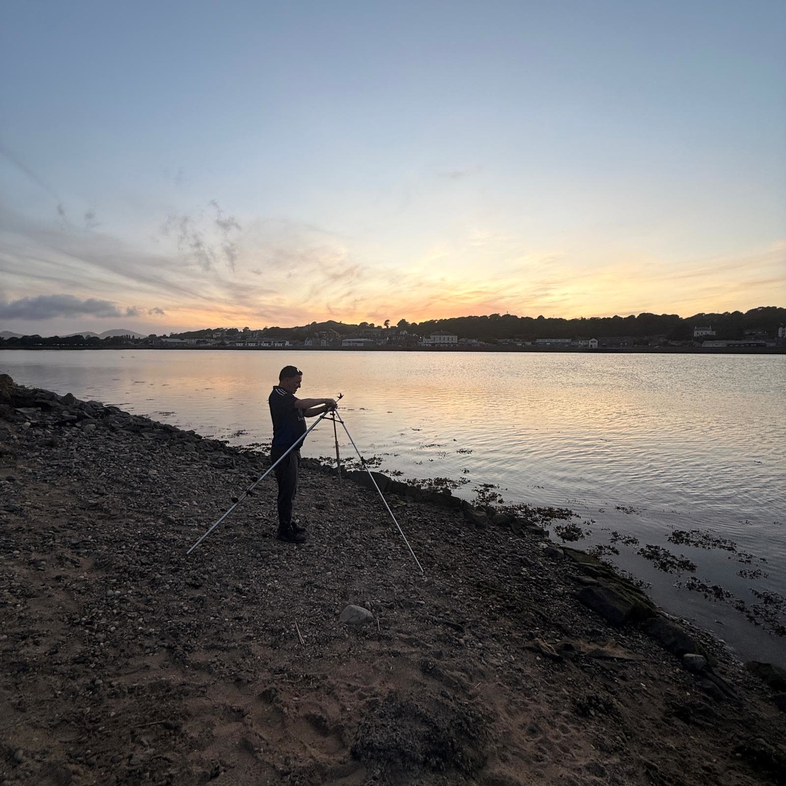 An angler fishing a North Wales estuary as the sun sets behind the hills