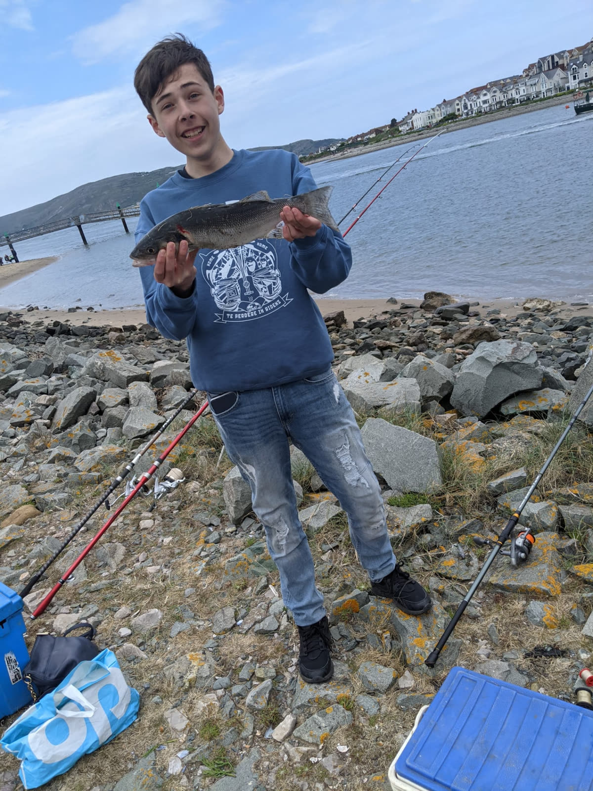 A young angler holding a bass caught from the rocks in North Wales